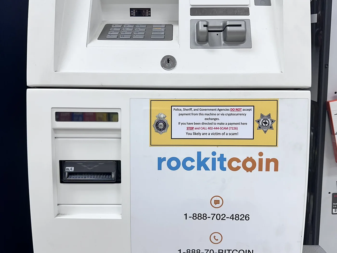 A cryptocurrency kiosk with a yellow warning sticker saying police, sheriff and government agencies do not accept payment from the machine, and that anyone told to pay there is likely a scam victim.